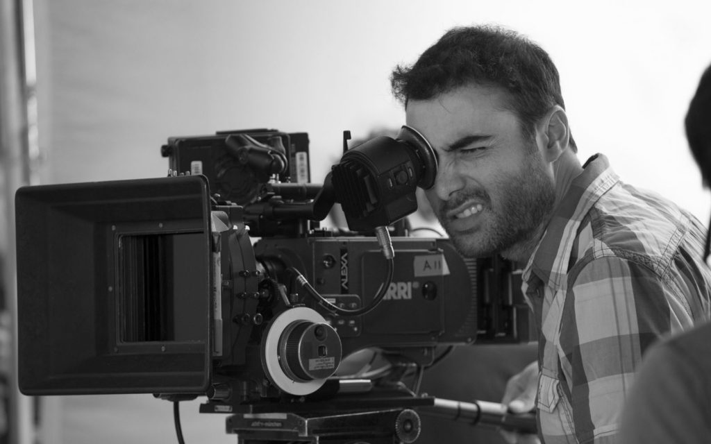 A man intently filming with a professional camera in black and white.
